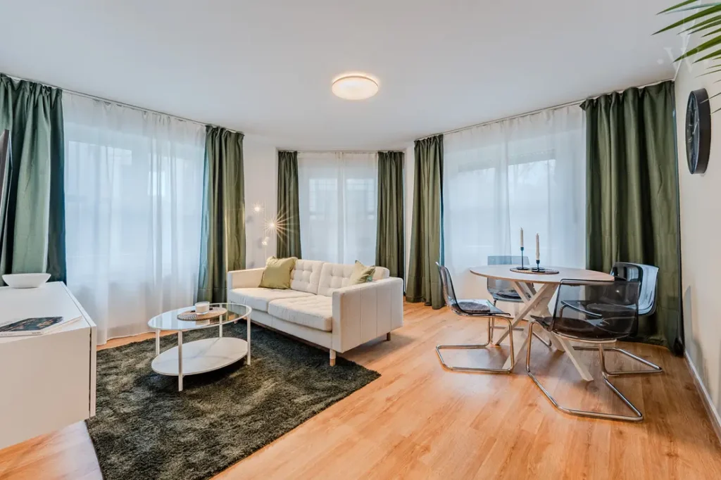 Bright living room with white sofa, dining table, green curtains and wooden floor.