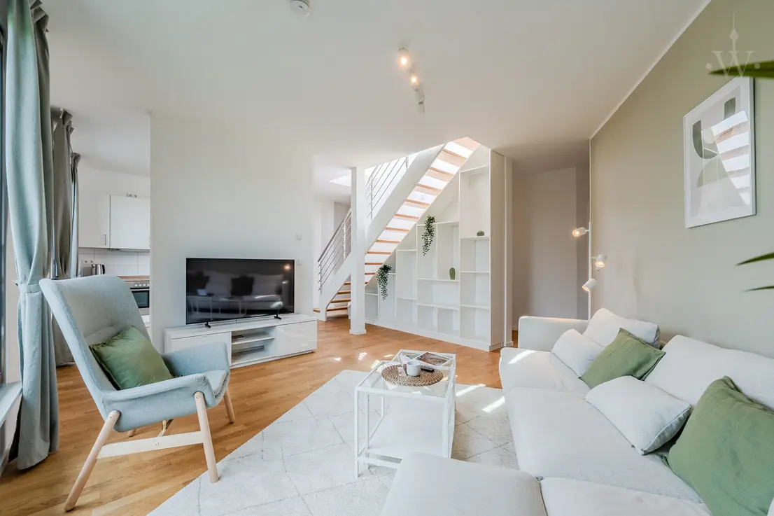 Bright, modern living room with cosy sofa, TV, staircase with wooden steps and decorative shelf