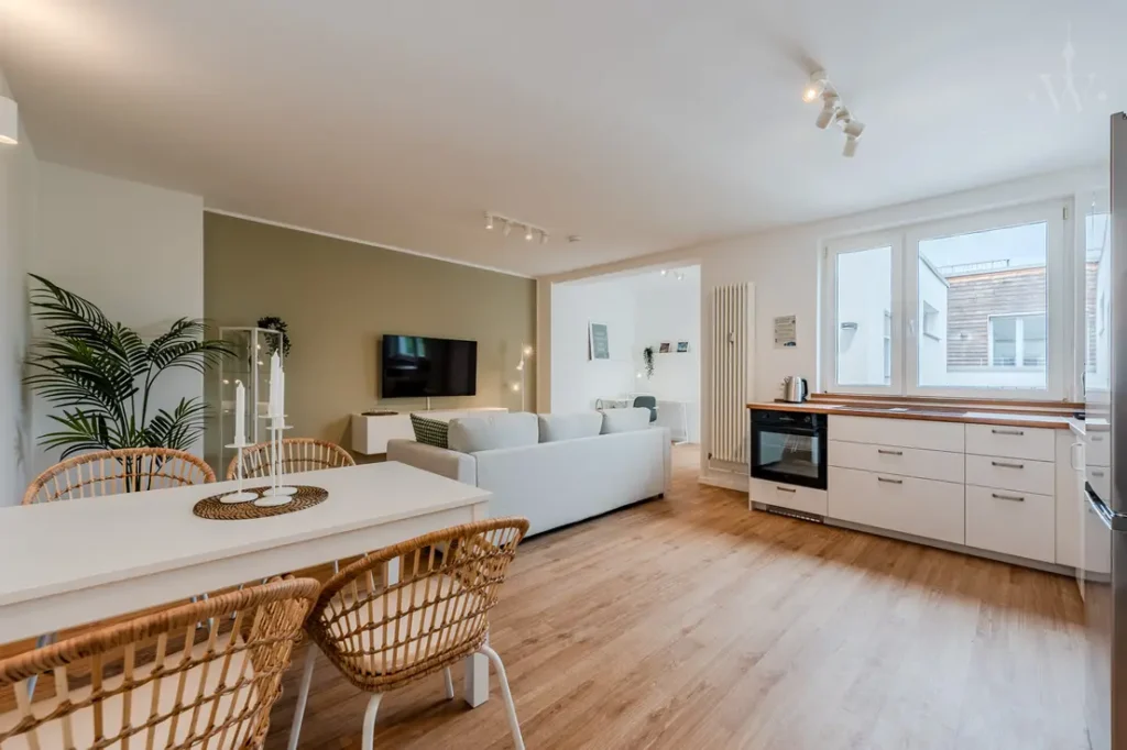 Offener Wohn-Essbereich mit Einbauküche, Esstisch und Holzfußboden, Blick zum TV.