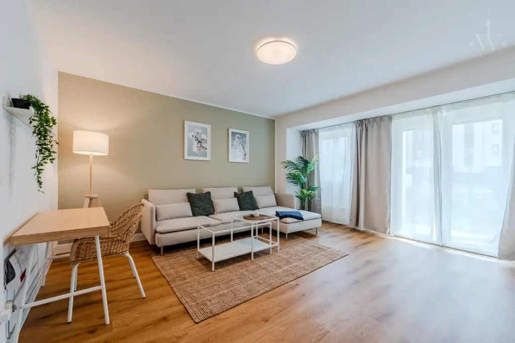 Helles Wohnzimmer mit zwei Sofas, Wandbildern, großer Fensterfront und Zimmerpflanze.