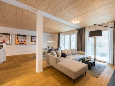 Offenes Wohnzimmer mit großem Ecksofa, Holzdecke und moderner Wandkunst im Berliner Apartment