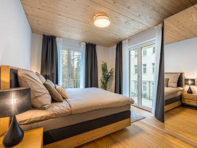 Schlafzimmer mit großem Bett, Vorhängen und Balkonzugang – hell und modern